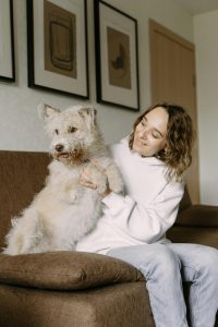 A woman holding her white dog whilst sitting on a sofa